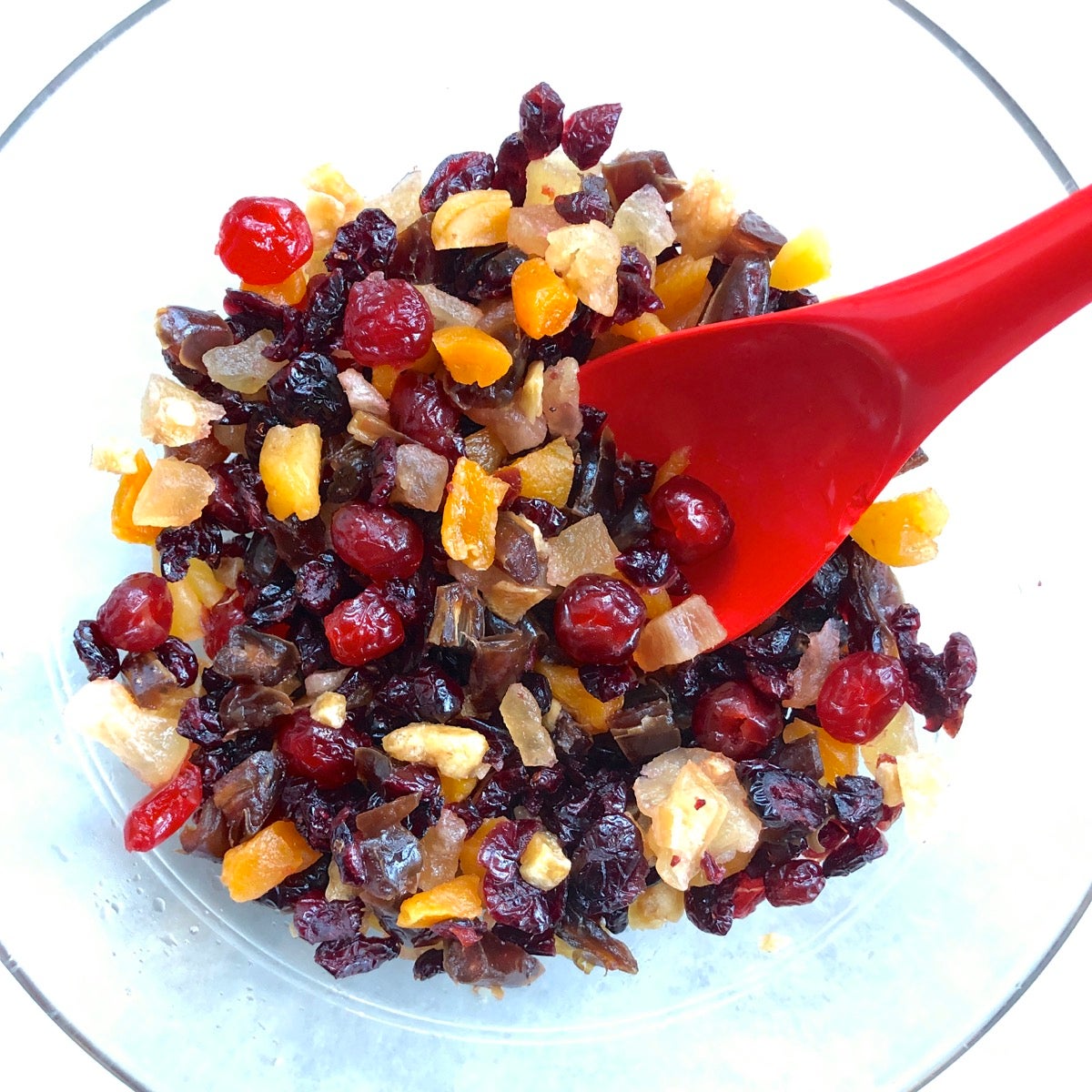 Choped dried fruit moistened with cranberry juice in a large bowl with a red spoon.